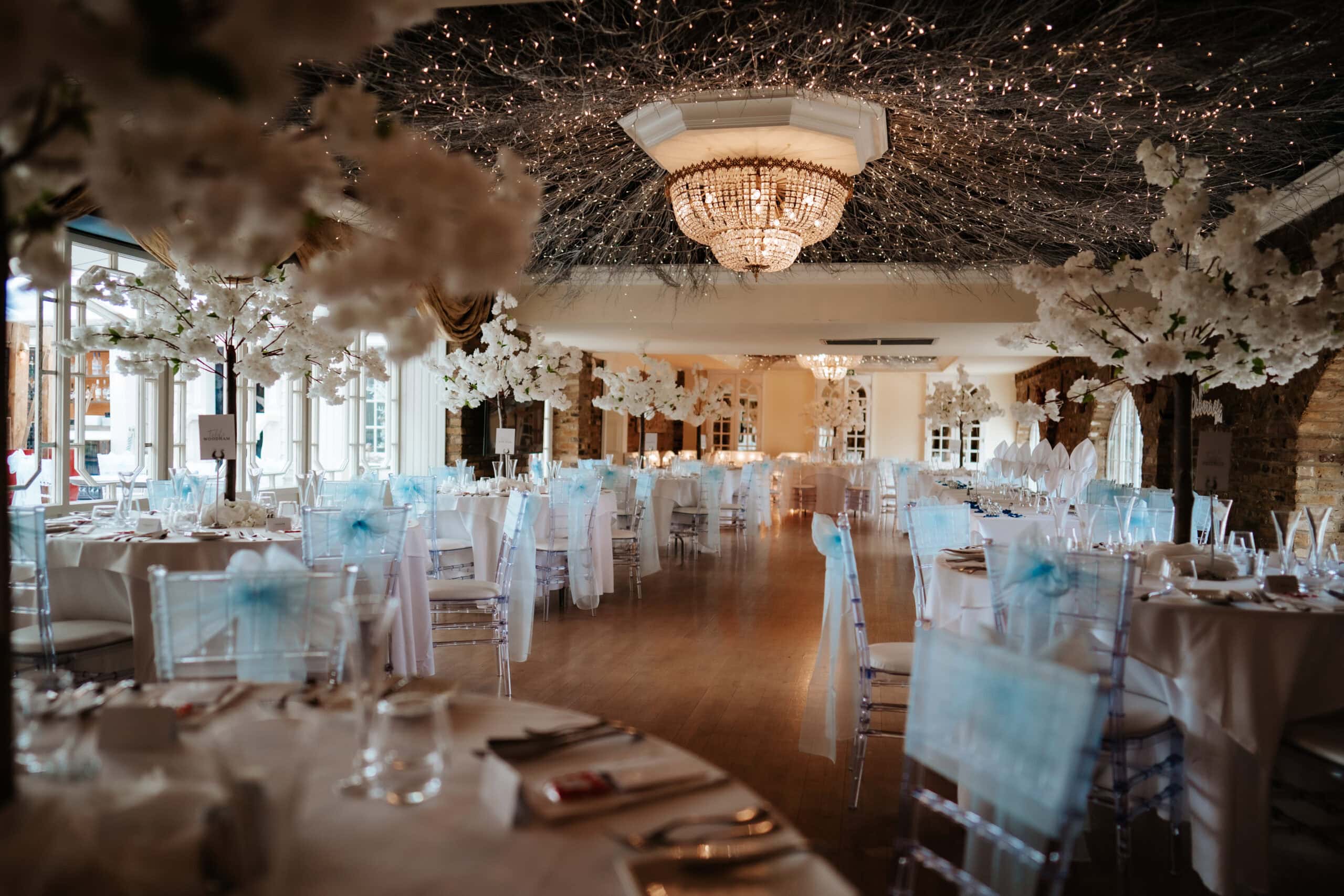 The banqueting suite at Friern Manor country hotel set for wedding reception with crystal chandelier and elaborate white blossom tree styling – photographed by Lily & White