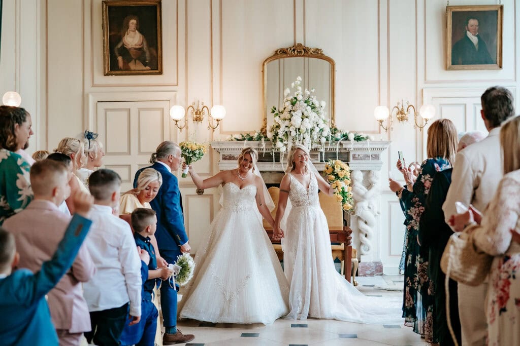 Wedding ceremony in the Queen's Gallery at Gosfield Hall with guests and natural light through tall windows — photographed by Lily & White