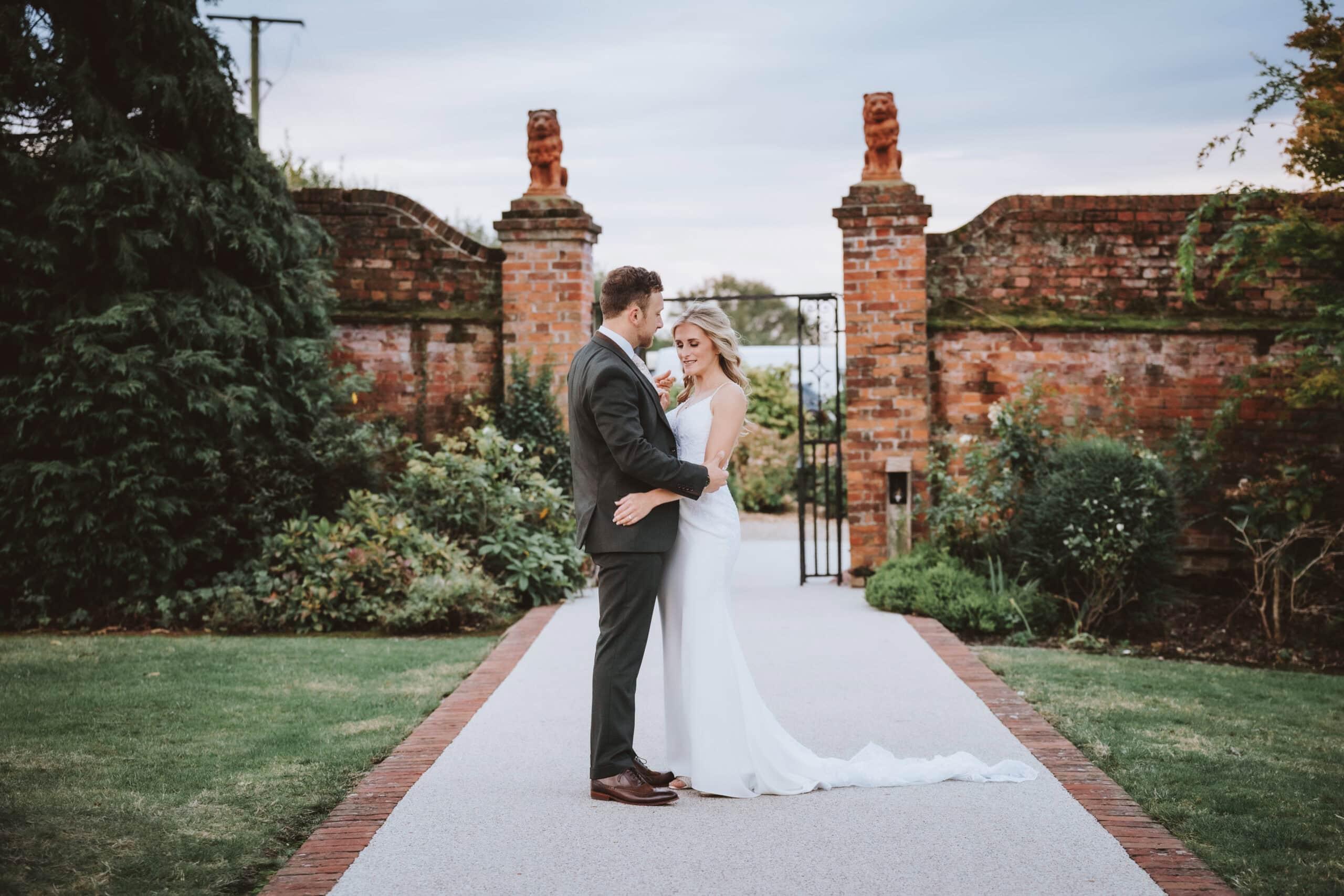 Emily and Harvey sharing a quiet moment together at the walled garden gates at Gaynes Park, Essex, on their late summer wedding day – 29th September 2024, photographed by Tel, Lily & White