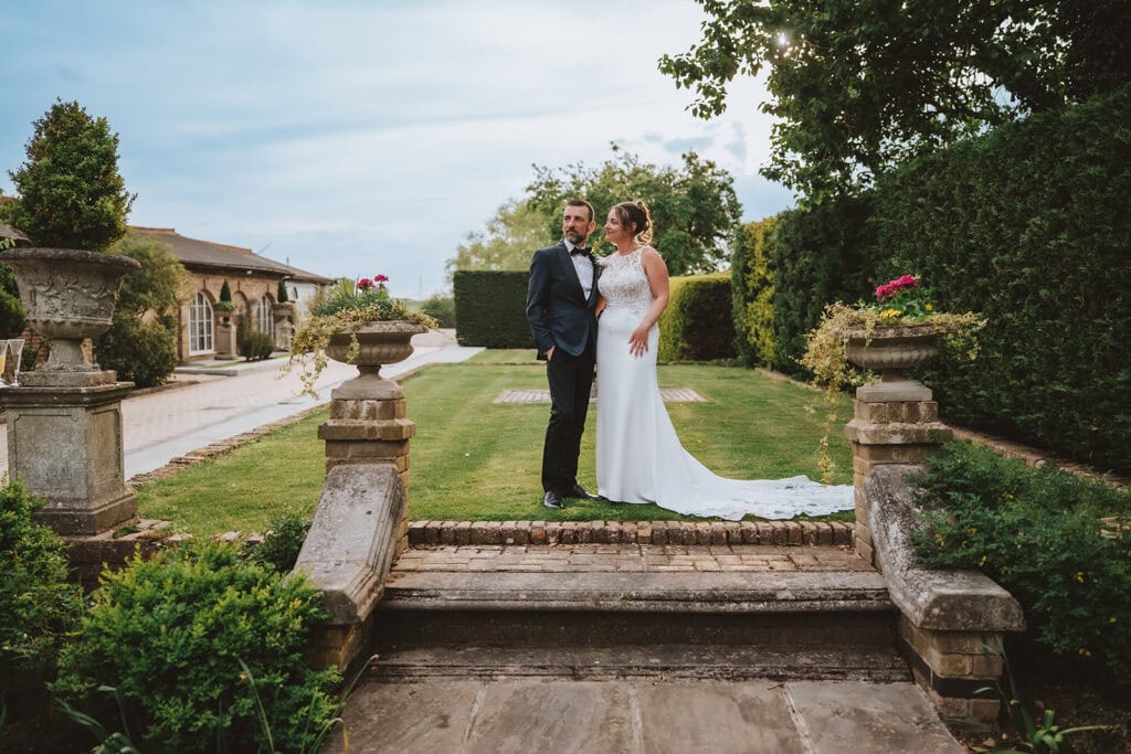 Bride and groom on the formal garden steps at Friern Manor with stone urns and manicured hedges in Brentwood, Essex – editorial wedding photography by Lily & White