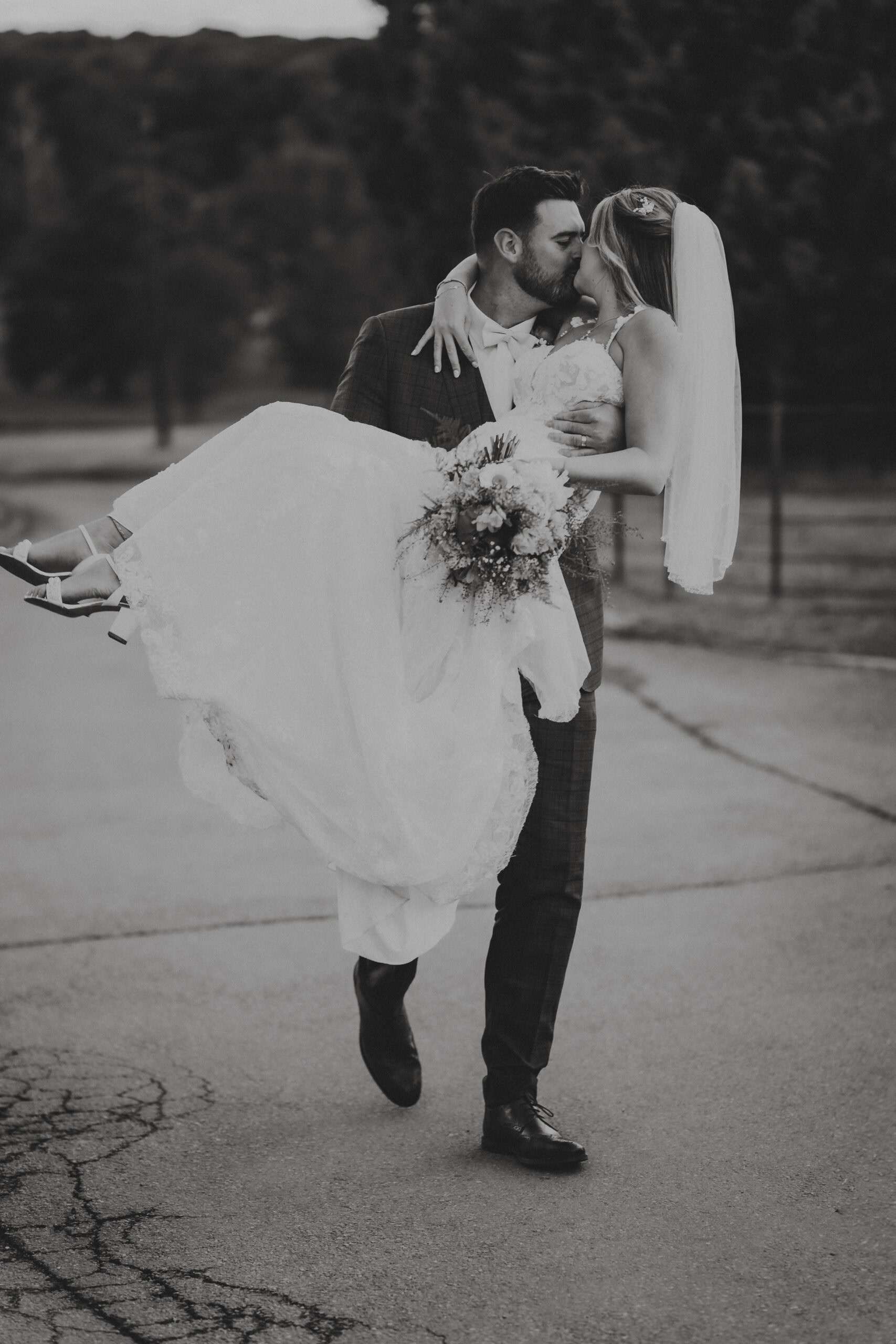 Cinematic black and white wedding photography in Essex, capturing a candid and joyful moment as a groom carries his bride during their editorial portrait session.