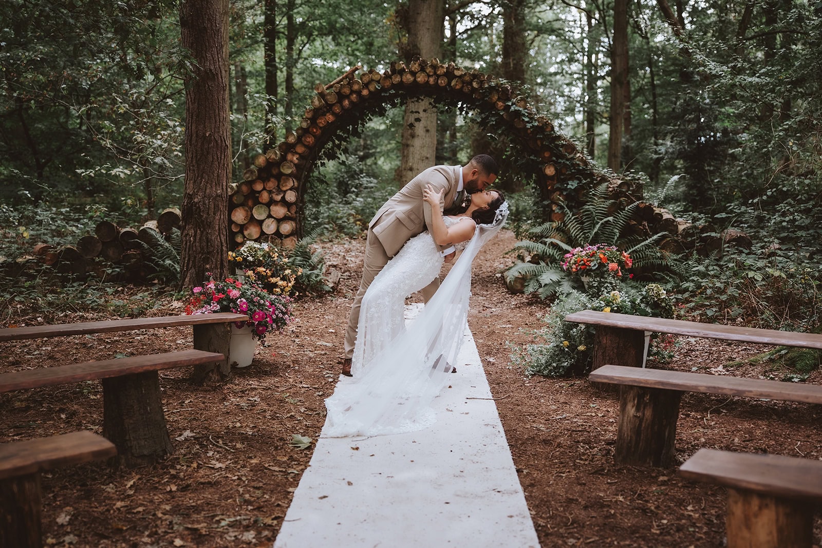 Newly married couple sharing a dip kiss down the woodland aisle at Captains wood barns wedding venue in essex