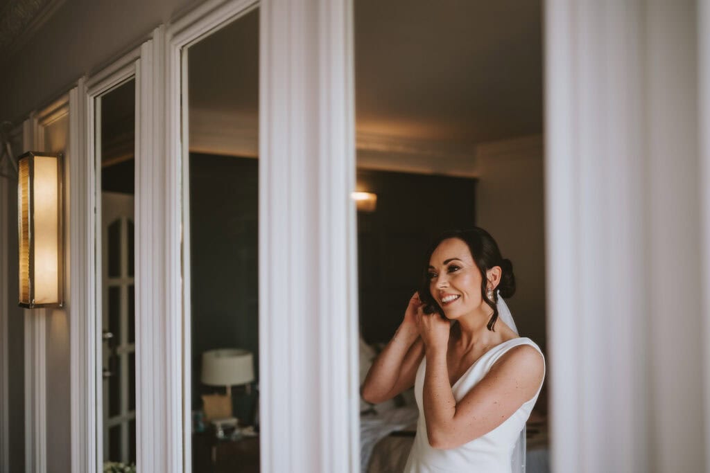 Bride looking in mirror during preparations at Friern Manor – documentary wedding photography by Lily & White