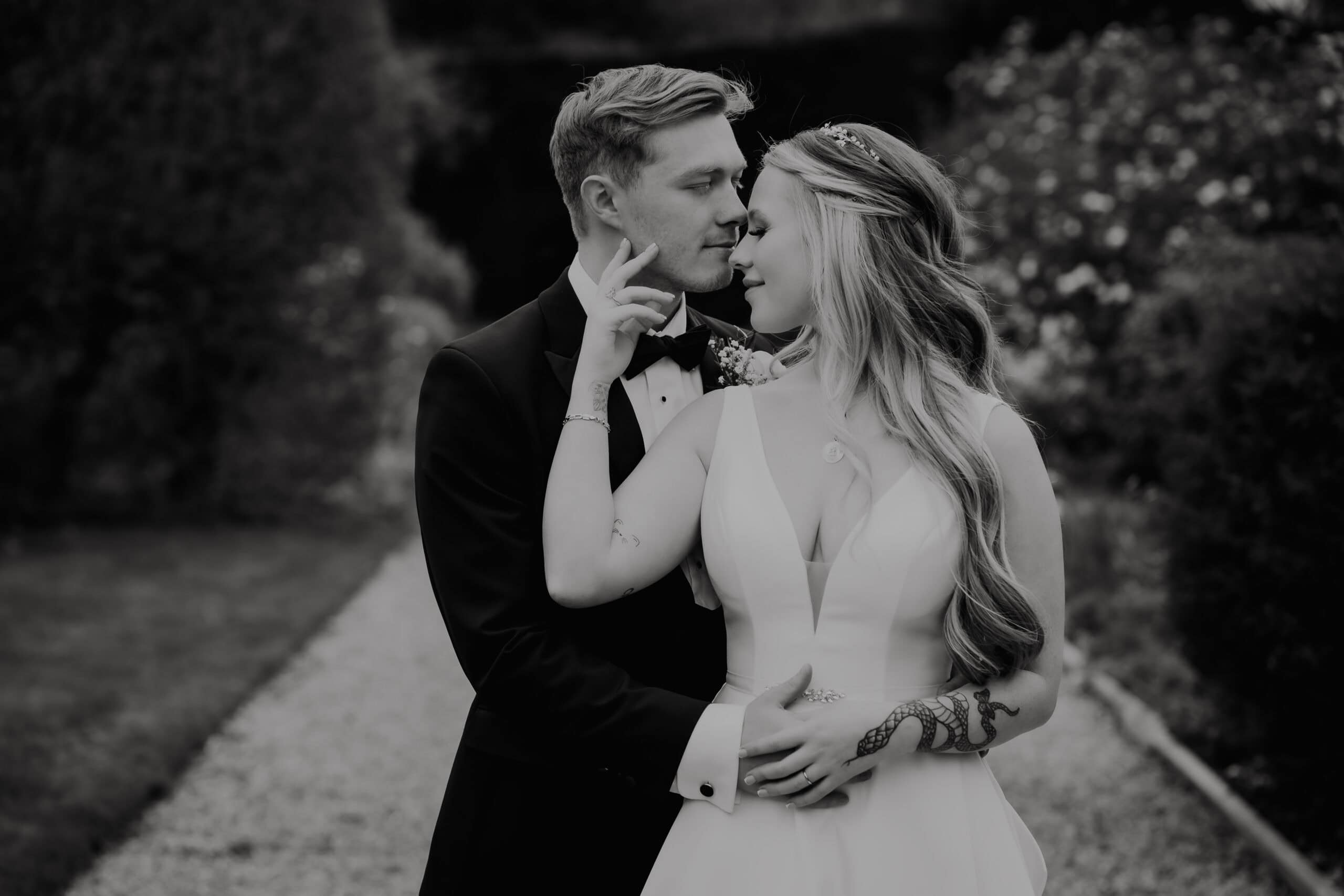 Olivia and Alfie in a close black and white portrait in the gardens at Gaynes Park, Olivia's hand resting gently on Alfie's face – wedding photography by Tel, Lily & White