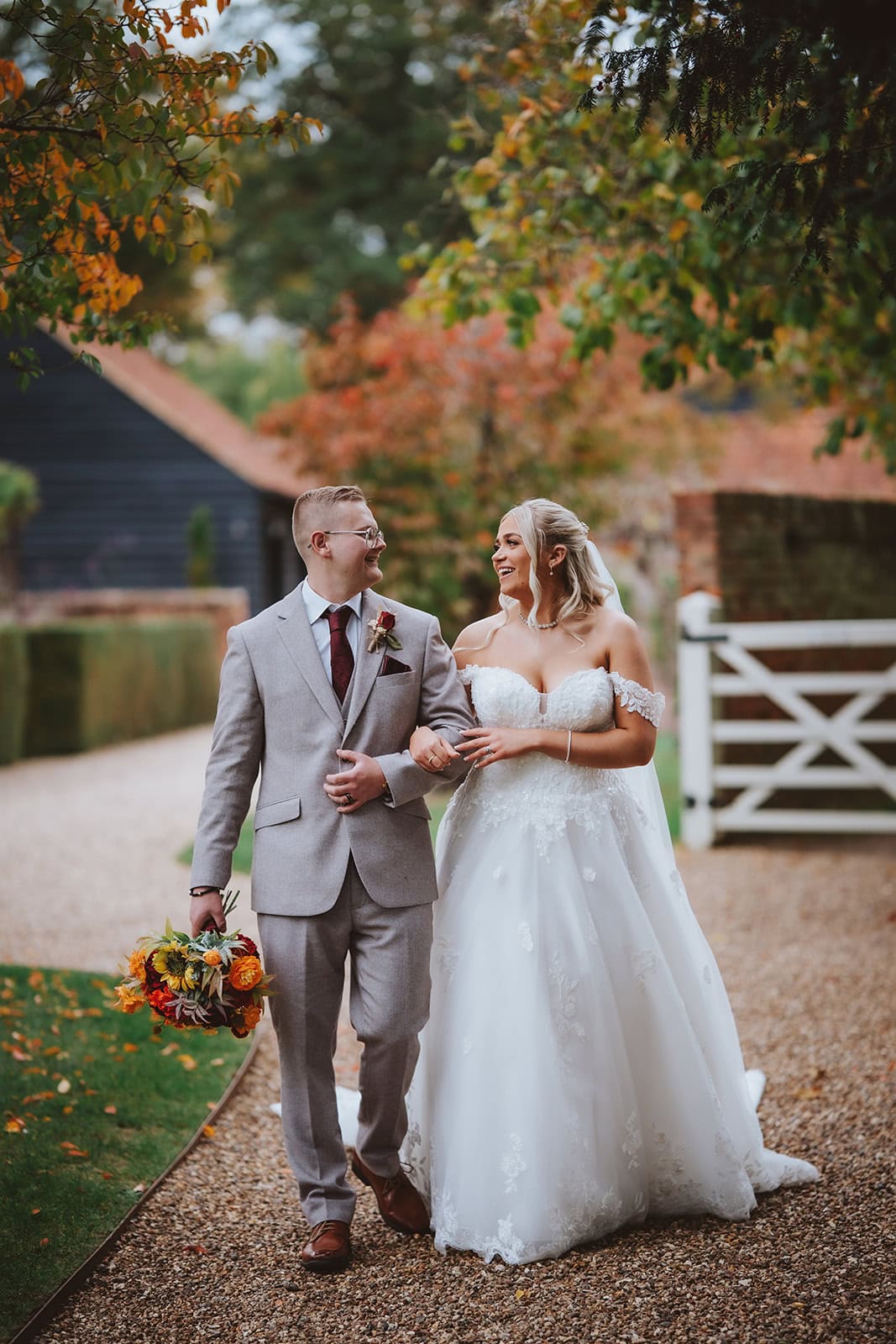 Editorial wedding photography at Blake Hall in Essex, featuring a bride and groom walking together through the venue's rustic grounds during an autumn wedding.