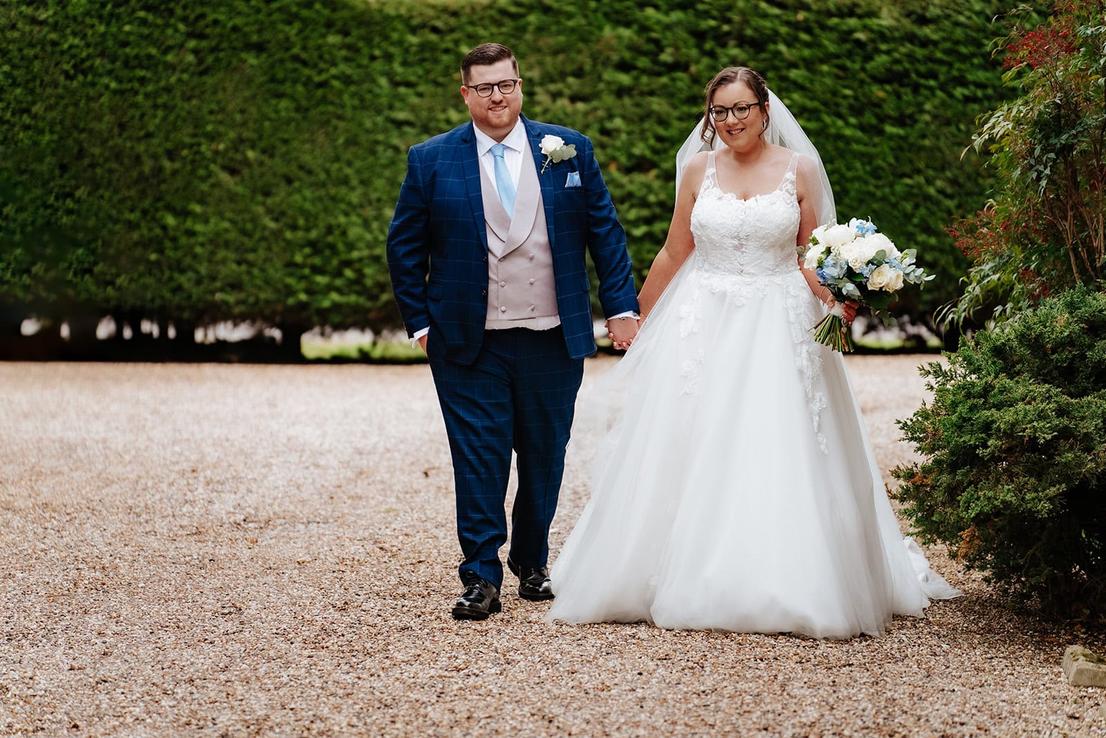Hollie and Lewis walking through the gardens at Friern Manor on their wedding day, spring light, Brentwood, Essex – photographed by Tel, Lily & White