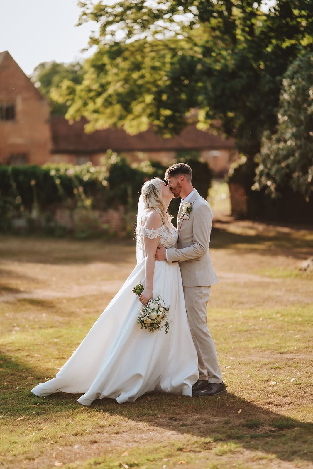 Bride and groom embracing in the gardens at Leez Priory wedding venue surrounded by summer blooms — editorial wedding photography by Lily & White