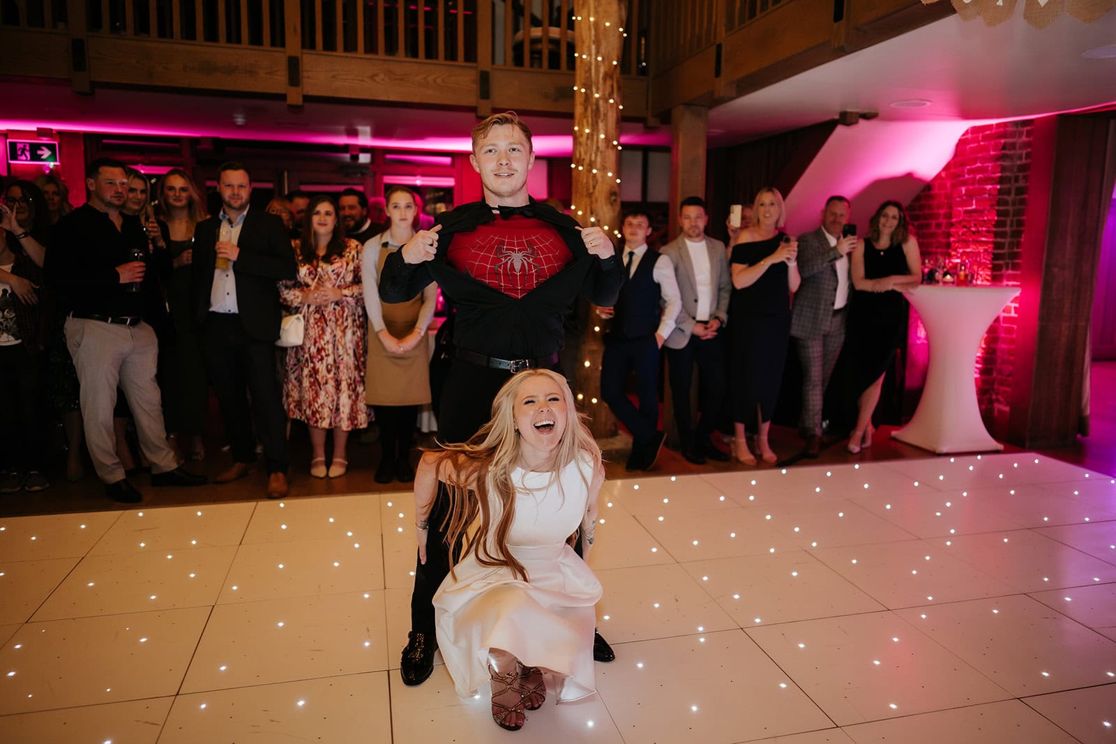 Alfie revealing a Spiderman suit beneath his shirt during the first dance at Gaynes Park's Mill Barn, Olivia laughing on the starlit dance floor as guests look on – wedding photography by Tel, Lily & White